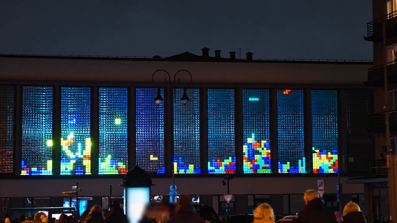 Nine glass-block windows lit with falling-blocks games at night