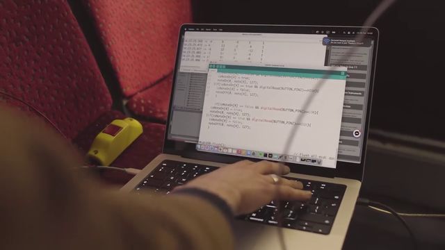 A hand typing on a laptop that shows code, set on a red bus seat